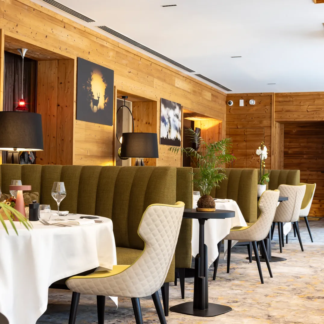 Restaurant avec des tables et des chaises disposées le long d'un mur en bois, des plantes et des lampes sur les tables