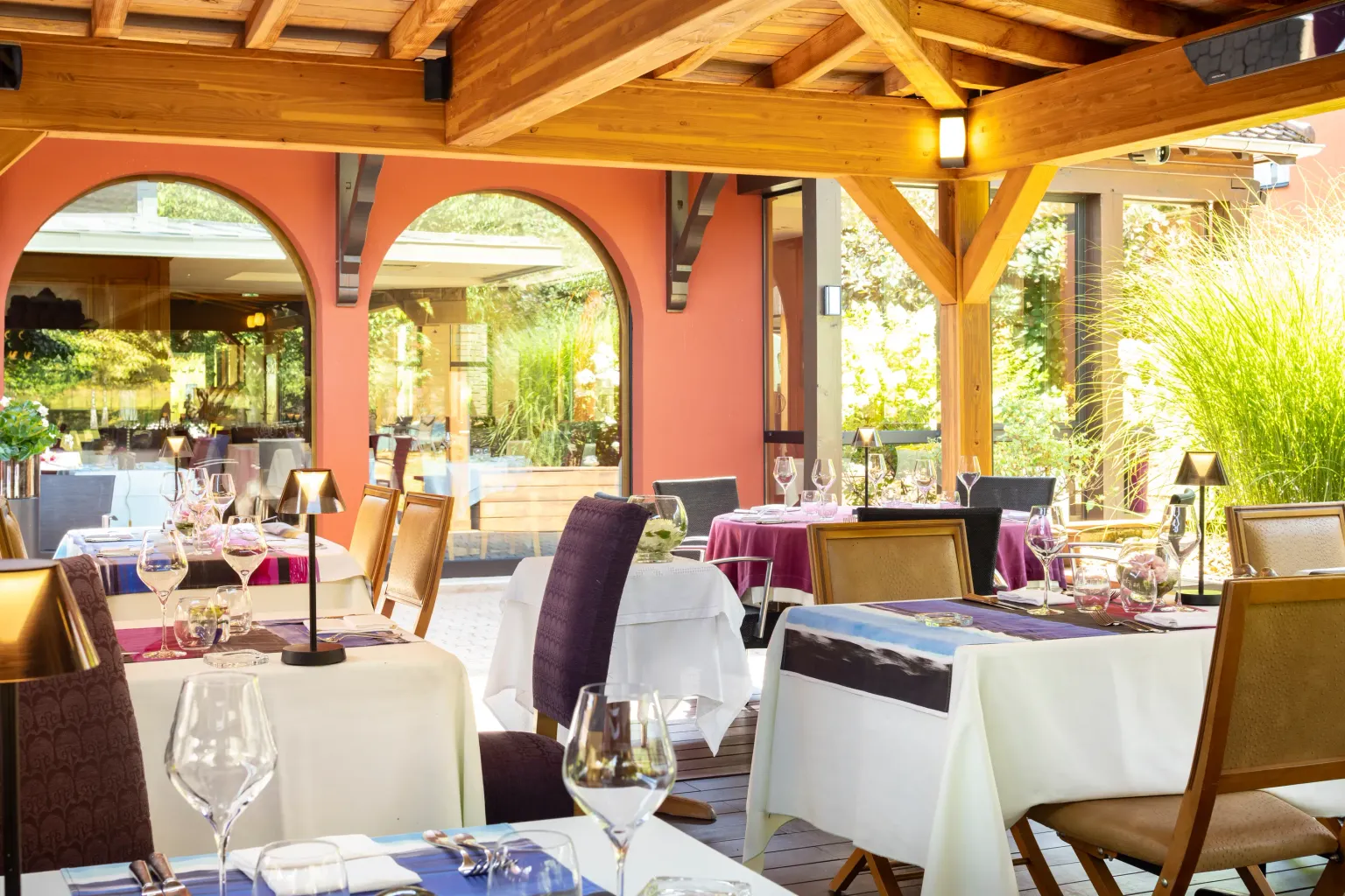 Terrasse de restaurant avec tables dressées, nappes blanches et verres à vin, sous une structure en bois avec arches orange