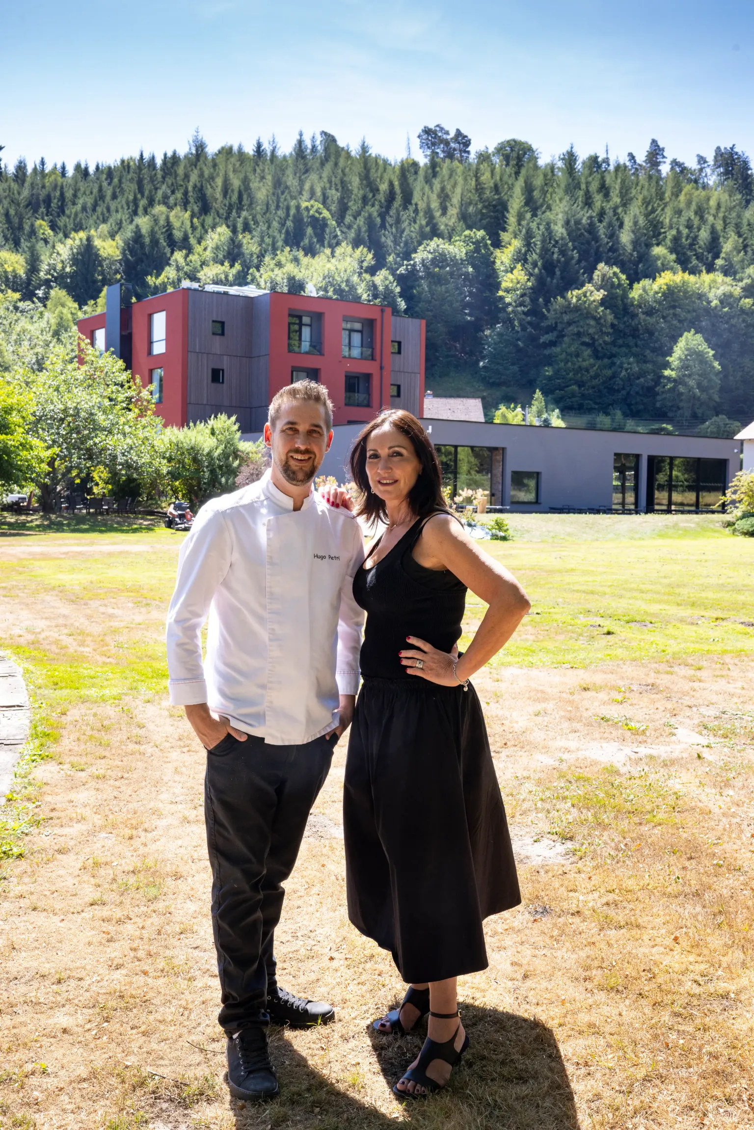 Un homme et une femme posent devant un bâtiment moderne entouré d'arbres et d'une pelouse