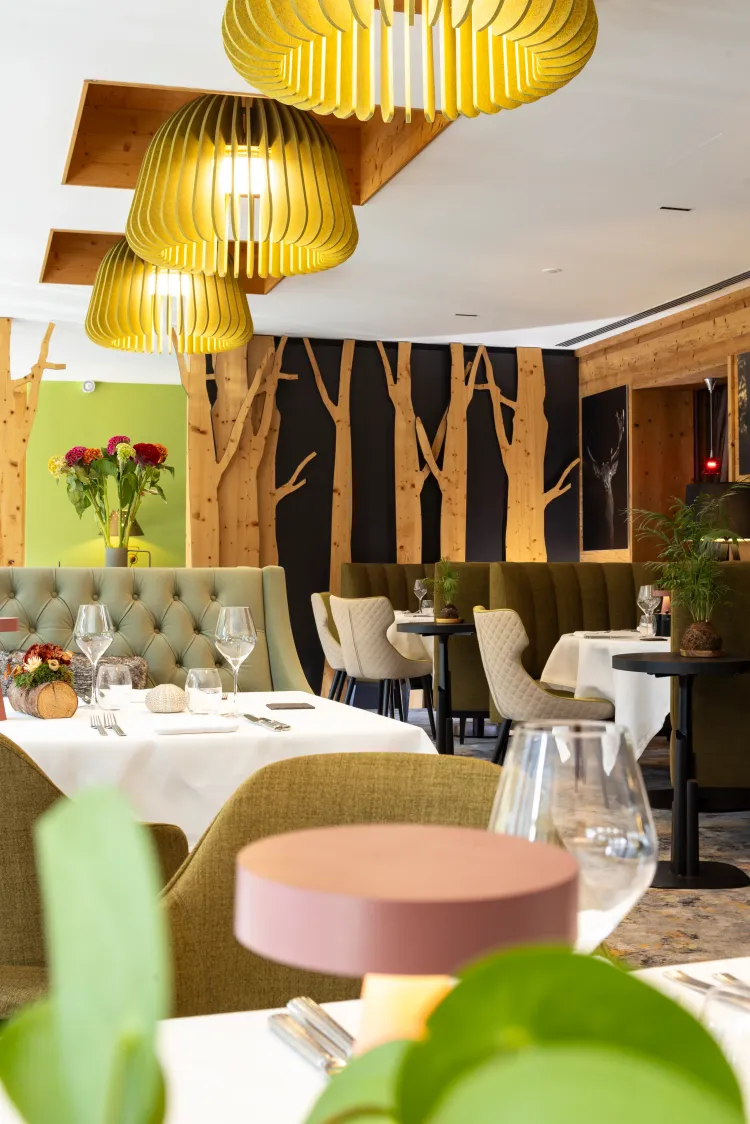 Restaurant élégant avec des tables dressées, des banquettes vertes et des suspensions lumineuses dorées, des murs en bois et des plantes décoratives