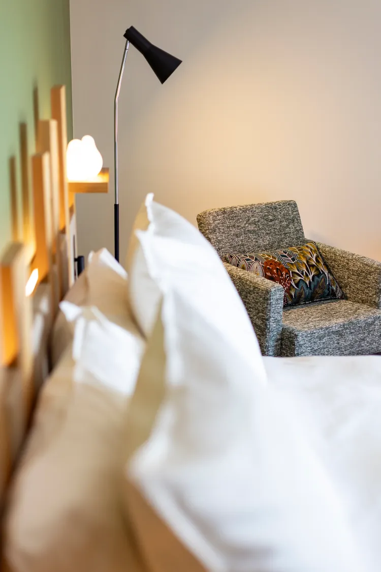 Un lit avec des oreillers blancs et un canapé gris avec un coussin décoratif, éclairés par une lampe de chevet